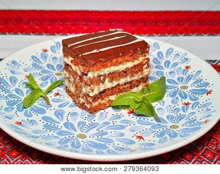 A Slice Of Cake With Nuts And Prunes In Chocolate Icing On A Plate, Decorated With Mint Leaves.
