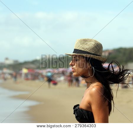 Beautiful Young Woman Meditates On The Beach With Her Eyes Closed And Her Hair In The Wind. The Sea