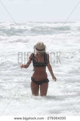 Beautiful Girl With Hat At The Sea Who Walking In The Water. The Sea In The Background. Sabaudia, La