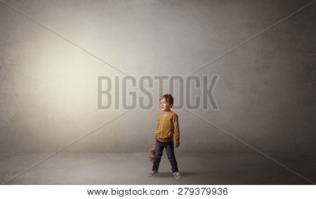 Little waggish kid staying alone in a big empty room with his plush