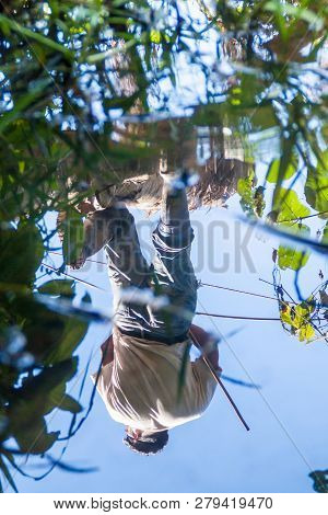 Madidi, Bolivia - May 8, 2105: Water Reflection Of A Native Tour Guide Hunting In A Jungle Of Madidi