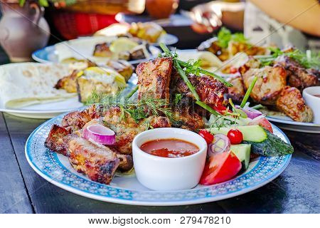 Grilled Ribs, With Slices Of Tomato And Cucumber With Tomato Sauce. Served On A Plate.