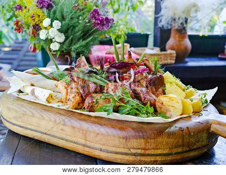 Fried Meat On A Wooden Board With Pita Bread, Baked Potatoes And Vegetables, Greens And Onions.