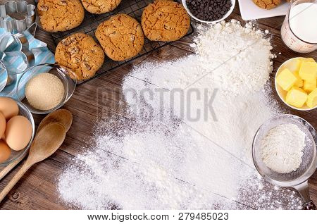 Freshly Made Chocolate Chip Cookies On A Dark Wood Table With Dusted Flour And Ingredients.