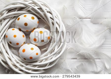 Eastr Eggs In The Nest And White Feathers On Wooden Table