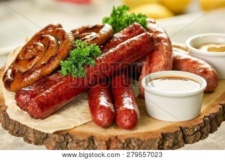 Assorted Grilled Sausages With Sauce On Rustic Round Wooden Board. Smoked Grilled Sausages With Sauc