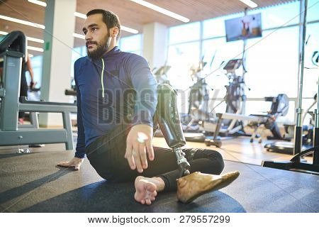 Bearded Athlete With Amputee Leg Sitting On The Floor And Resting In Health Club