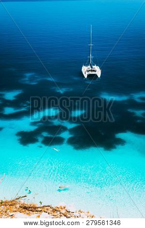 White Catamaran Yacht Drift On Clear Azure Water Surface In Calm Blue Lagoon With Transparent Water 