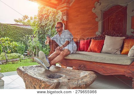 Man Using Smart Phone On A Terrace Sofa In Summertime.