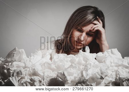 Sick young woman with a runn nose covered by many paper tissues.