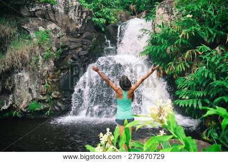Hawaii travel nature waterfall woman hiker at Canyon Trail Waipoo Falls in Waimea, Kauai island, USA. Freedom happy girl with open arms meditating yoga in rainforest.