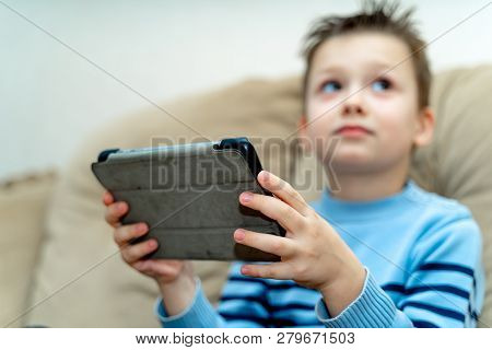 Chlid Holding Pc Tablet While Sitting On A Couch And Looking Up Aside. Boys Hands With A Wireless Ta