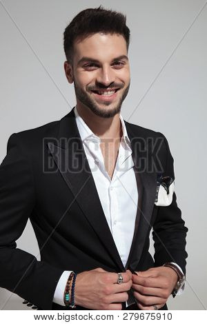 portrait of happy smart casual man unbuttoning black suit while standing on light grey background