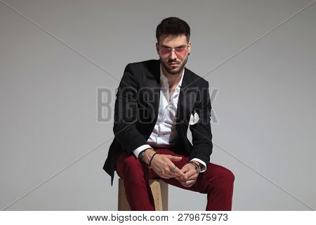 portrait of smart casual man wearing red sunglasses sitting on wooden crate and holding hands together