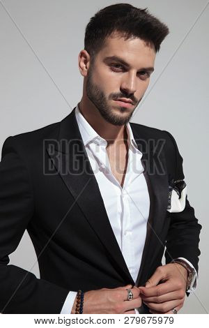 portrait of handsome fashion man buttoning black suit while standing on light grey background