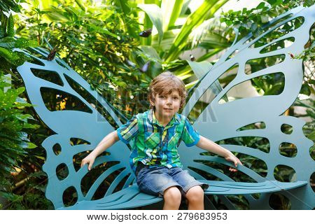 Little Blond Preschool Kid Boy Discovering Flowers And Butterflies At Botanic Garden. Schoolchild In