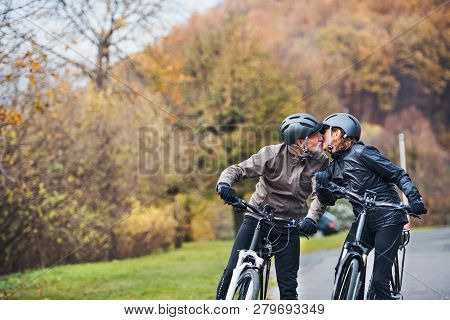 Active Senior Couple With Electrobikes Standing Outdoors On A Road In Nature, Kissing.