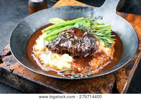 Traditional German braised veal cheeks in brown sauce with mashed potatoes and beans as closeup in a wrought-iron pan