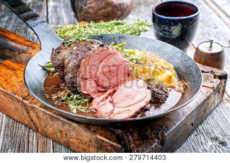 Barbecue roast boar joint with roesti and game red wine sauce as top view in a wrought-iron pan