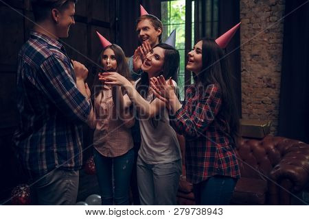 Group Of Cheerful Friends In Party Hats Sing Birthday Song And Congratulate Their Frinds With A Smal