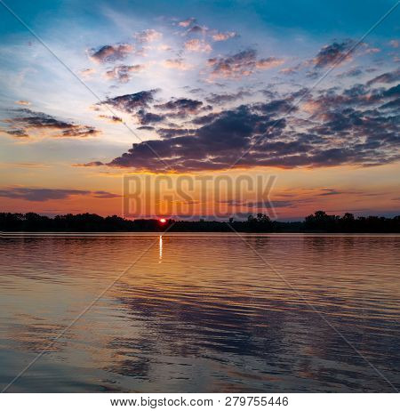 Sunset Behind Coastal Trees Against The Background Of The River And Clouds.