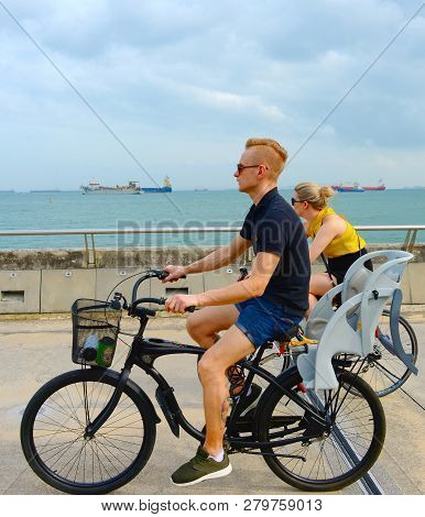 Singapore - February 6, 2017: Couple Riding Bycicles At Singapore Harbor. Singapore Is Major Financi
