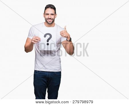 Handsome young man holding paper with question mark over isolated background happy with big smile doing ok sign, thumb up with fingers, excellent sign
