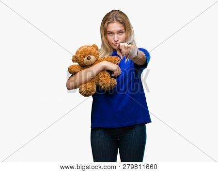 Young caucasian woman holding cute teddy bear over isolated background pointing with finger to the camera and to you, hand sign, positive and confident gesture from the front