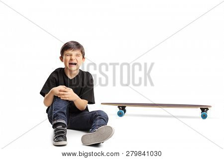 A boy with an injured knee sitting next to a longboard isolated on white background
