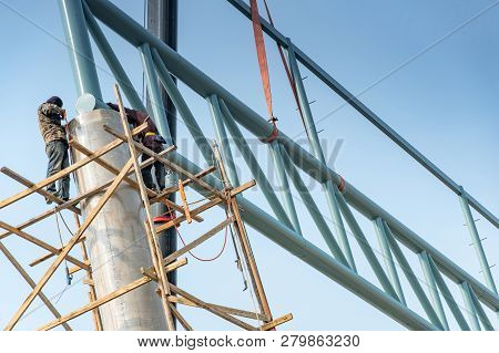 Male Construction Workers Standing On Wooden Scaffolding Welding Steel Truss Structure On Concrete C