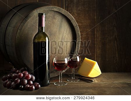 Bottle Of Red Wine With Glasses And Cheese On Wooden And Barrel Background.