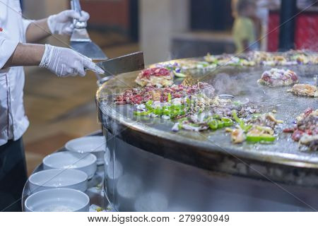 Cooking Street Food On A Large Firebox. Frying Meat And Seafood On The Brazier In The Street. A Cook