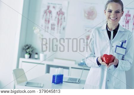 A doctor with stethoscope examining red heart, isolated on white background