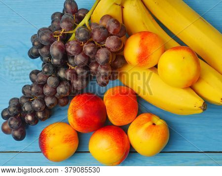 Ripe And Beautiful Fruits, Bananas, Grapes And Apricots On A Blue Wooden Background. Proper Nutritio