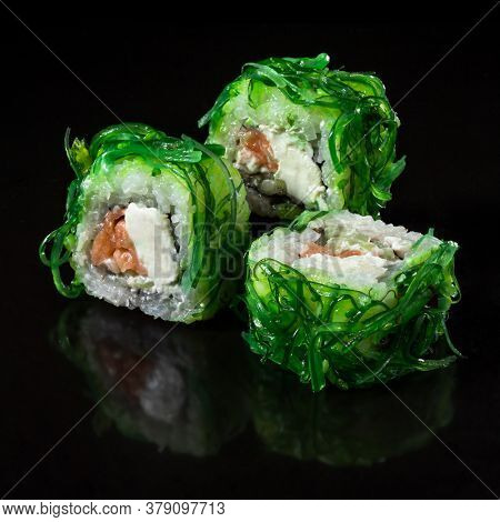 Imperator Sushi roll with seafood and Chuka. Sushi roll with Chuka, salmon, cucumber, and cream chease over  black backgraund.