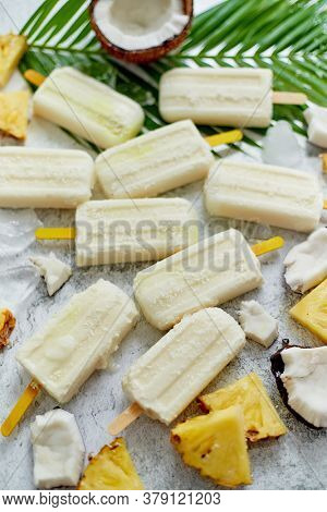 Summer popsicles on stick. Pinacolada flavour. Made with pineapple, cocount milk and rum. Vegan snack. Decorated with fresh fruit. Top view. Flat lay.