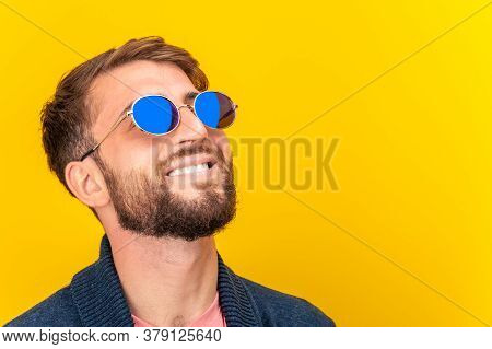 Close Up Portrait Of Funky Young Bearded Hipster Man In Blue Sunglasses Smiling Brightfully On A Yel