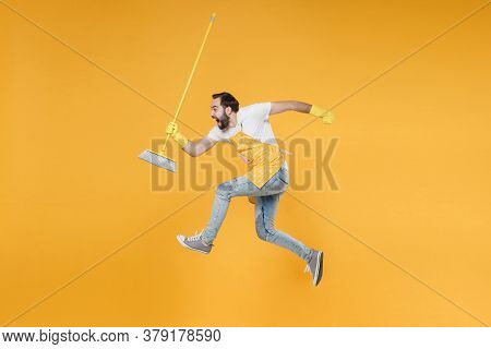 Side View Of Crazy Young Man Househusband In Apron Rubber Gloves Hold In Hands Broom While Doing Hou