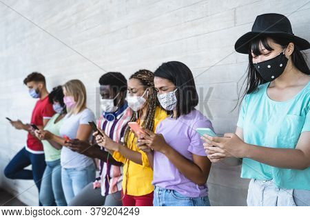 Young People Wearing Face Mask Using Mobile Smartphone Outdoor - Multiracial Friends Having Fun With