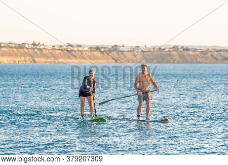 Mature Couple On Sup, Stand Up Paddle Board, Having Fun On Quiet Sea At Sunset