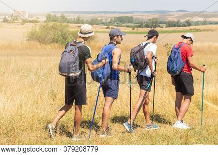 Four Young People With Trekking Poles Doing The Camino De Santiago In Spain And Arriving At The Vill