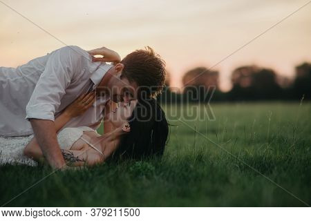 A Loving Couple Lies And Makes Love Among The Lawn At Sunset. Copy Space.