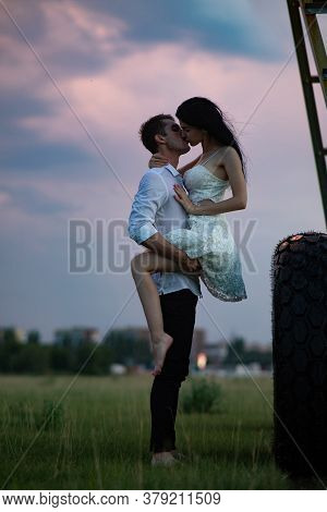 A Loving Couple Makes Love On Farm Near Agricultural Sprayer At Sunset.