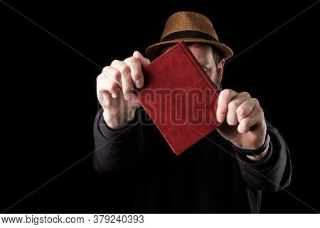 A White Bearded Man In A Hat Holds A Book In Front Of Him With Both Hands, Defends Himself Like A Sh