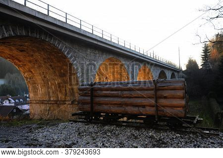 Wooden Cargo On Rail Vehicle Under A Railway Bridge, Lighted Tunnel Arches