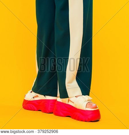 Women's Legs In Sport Sandals With Red Soles And Green Pants With Stripes On A Yellow Background.