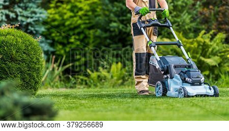 Professional Caucasian Gardener In His 40s Trimming Grass Lawn Using Modern Electric Cordless Mower.