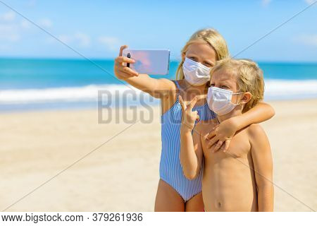 Funny Kids Taking Selfie Photo By Smartphone On Tropical Sea Beach. New Rules To Wear Cloth Face Cov
