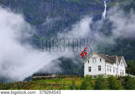 Ullensvang Town In Norway. Misty Mountains And A Waterfall. Norwegian Landscape.