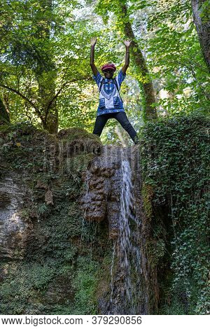 African Woman Stands Happy On The Top Of A Waterfall At A Hot Day In Summer. Linner Waterfall Is The